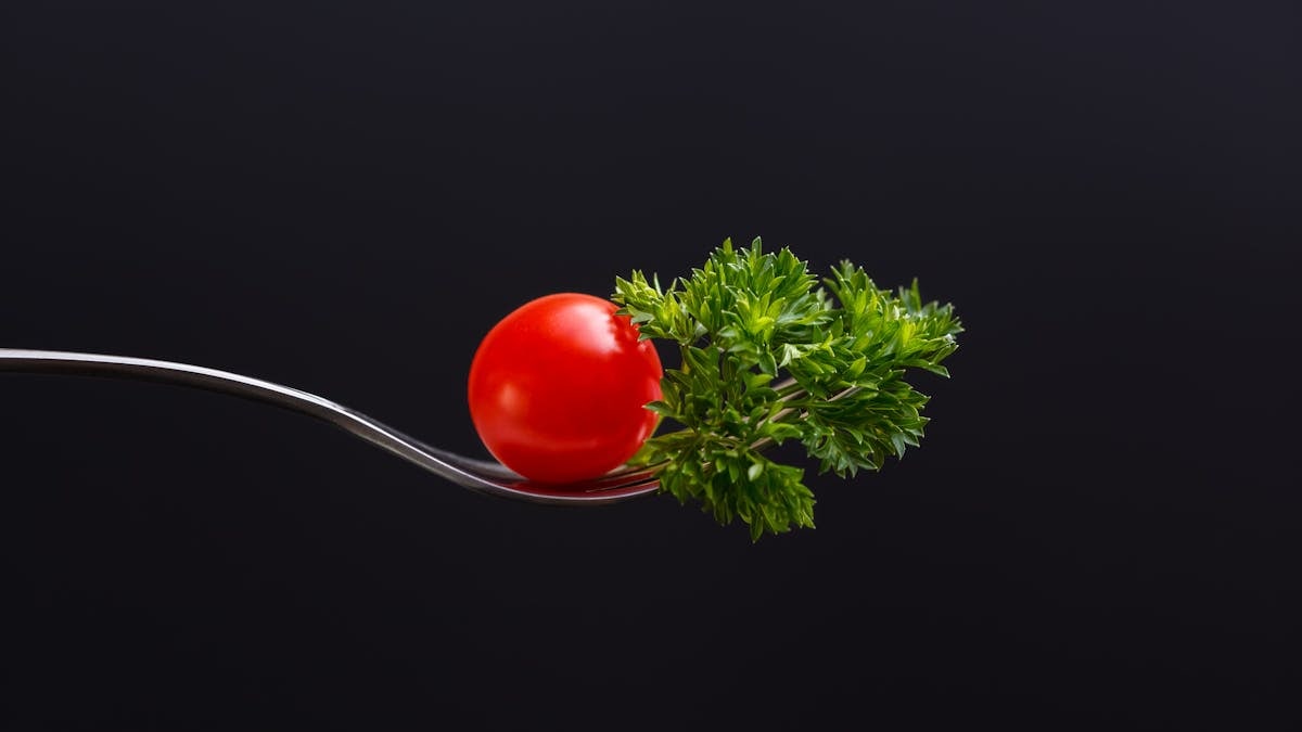 Composition of ripe red cherry tomato and green parsley on fork representing concept of healthy food